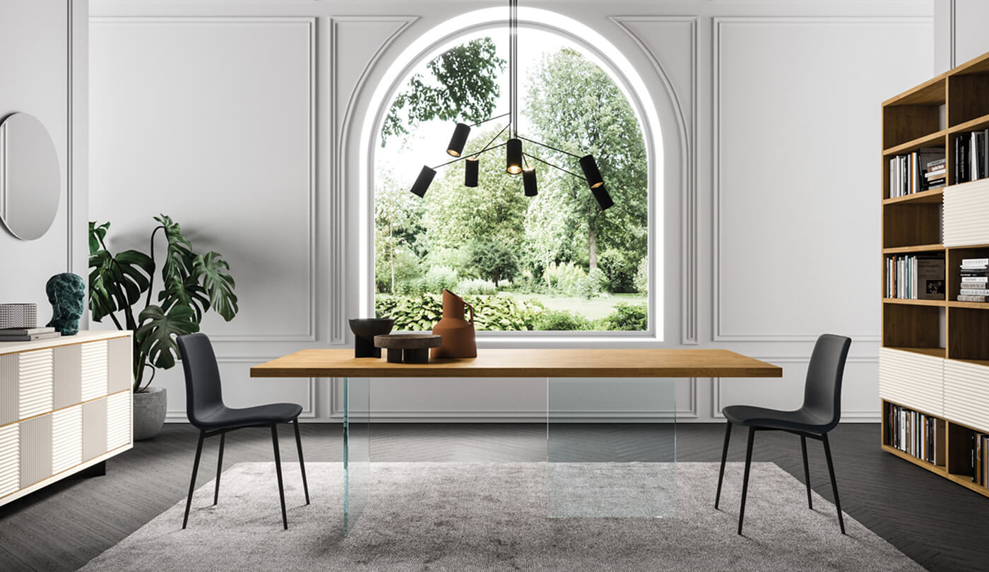 Tavolo con piano in legno e gambe in vetro, abbinato a sedie nere senza braccioli